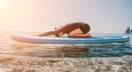 Yoga Paddleboard Pose Ocean Woman - A woman does yoga on a paddleboard in the ocean. The pose is a forward fold. The sun is shining and the water is calm.の写真素材