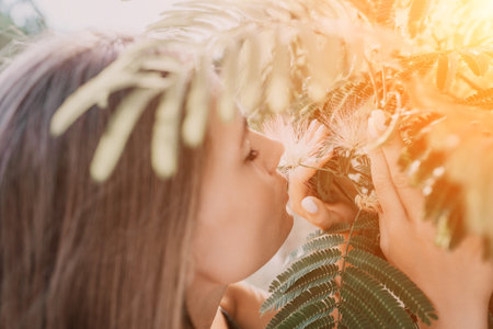 Beauty portrait of happy woman closeup. Young girl smelling Chinese acacia pink blossoming flowers. Portrait of young woman in blooming spring, summer garden. Romantic vibe. Female and natureの写真素材