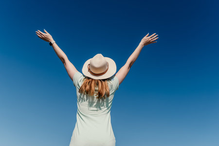 Woman in a Straw Hat with Arms Raised Against a Blue Sky