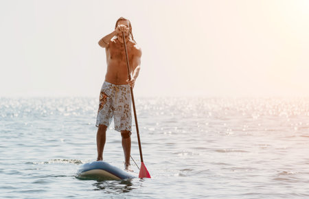 Man Paddleboarding Water Drinking - Man enjoys a refreshing drink while paddleboarding on calm...