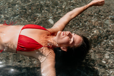 Woman Red Bikini Sea Relaxing: A woman in a red bikini relaxes in the shallow sea, floating on her back with her eyes closed.の写真素材