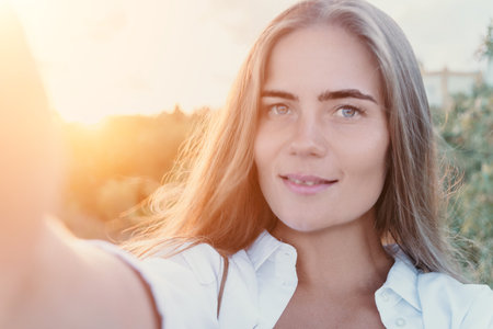 Woman Selfie Sunset Portrait - A young woman takes a selfie outdoors during sunset.の写真素材