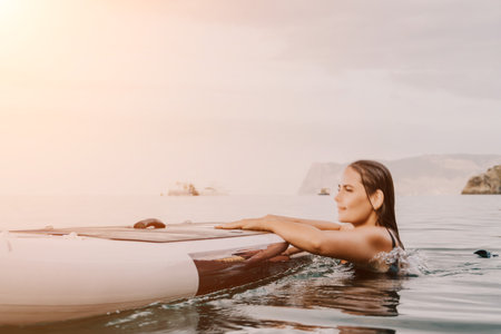 Woman Paddleboard Ocean Water Sports - A woman in a swimsuit is lying on her paddleboard in the ocean, looking to the right.の写真素材