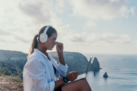 Woman Laptop Headphones Cliffside Ocean View Working Remotelyの写真素材