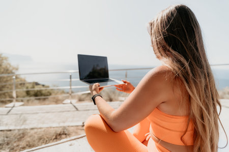 Woman in Orange Sportswear Using Laptop with a Sea Viewの写真素材