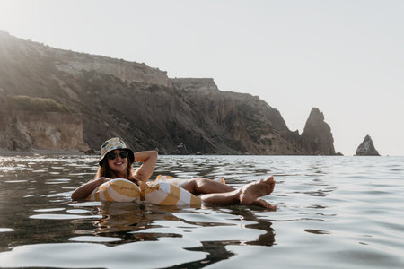 Woman, Beach, Relaxation: Woman sunbathing on an inflatable float in the sea near a rocky coastline.の写真素材