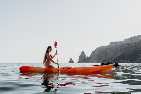 Kayaking Woman Ocean Coastline - Woman paddles kayak on calm ocean near rocky coastline.の写真素材
