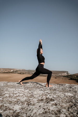 Woman in Black Yoga Outfit Practicing a Pose on a Cliff Topの写真素材