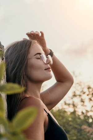 Woman Glasses Sunlight - A woman wearing glasses shields her eyes from the sun while standing...