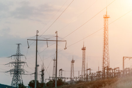 High voltage electric distribution network at sunset. Power transmission lines on supports with...