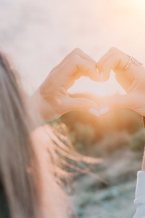 A womans hand is holding a heart shape, with the sun shining on it. Concept of love and warmth, as the sun symbolizes happiness and positivity. The heart shape represents the bond between two people.の写真素材