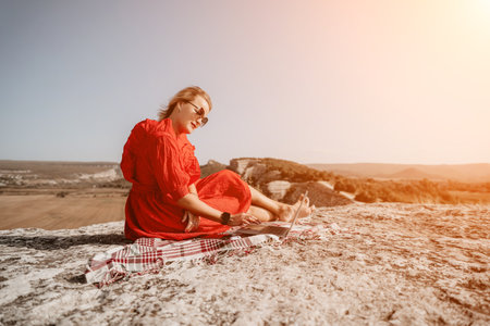 Woman in Red Dress Working on Laptop on a Rocky Hilltopの写真素材