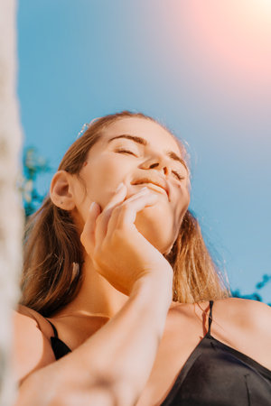 Woman Sunbathing Relaxing Summer - Close-up of a young woman with her eyes closed and hand on her cheek, basking in the warm summer sun.の写真素材