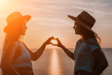 Silhouettes of Two Women Making a Heart Shape with Their Hands at Sunsetの写真素材