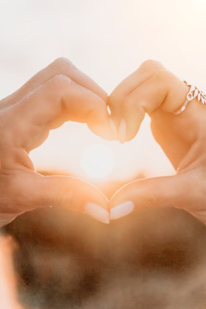 Hands Heart Shape Sunset Love Symbolism - A close-up image of two hands forming a heart shape with the setting sun in the background. This image is a classic representation of love, hope, and positivity.の写真素材