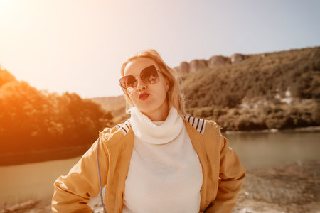 Woman Sunglasses River - Blonde woman wearing sunglasses and a jacket poses by a river in a mountainous landscape.の写真素材