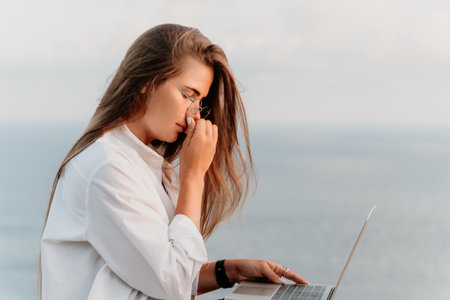 Woman Laptop Beach Working Outside - A woman works on a laptop outside on a beach.の写真素材