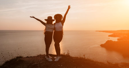 Silhouettes of Two Friends on a Cliff at Sunsetの写真素材