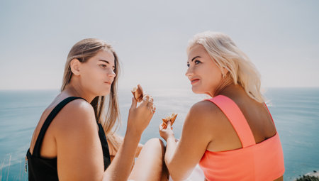 Two Women Relaxing by the Ocean, Enjoying Snacksの写真素材