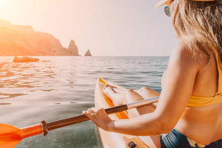 Kayaking Woman Sea Coastline - Woman paddling kayak on calm ocean with rocky coastline in...