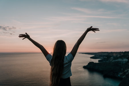 Silhouette of a Woman with Arms Raised at Sunsetの写真素材