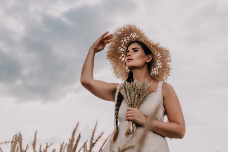Woman in a Straw Hat Looking Up at the Sky in a Wheat Fieldの写真素材