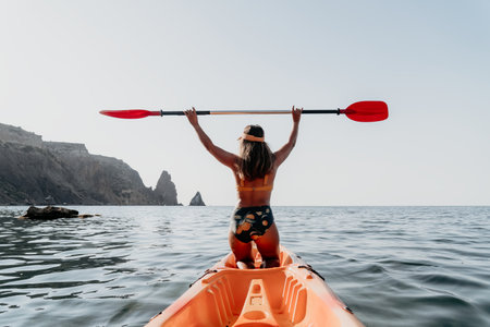 Kayaking, Ocean, Woman: Kayaking woman on the ocean with a paddle raised in the air, mountains in the background.の写真素材