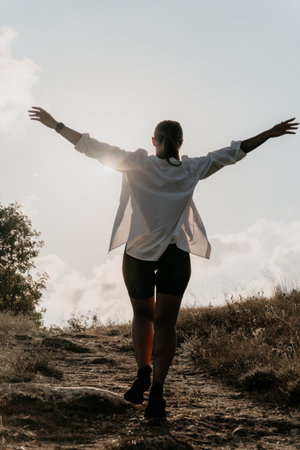 Woman Freedom Happiness - Backlit silhouette of a woman with arms outstretched walking on a trail.の写真素材