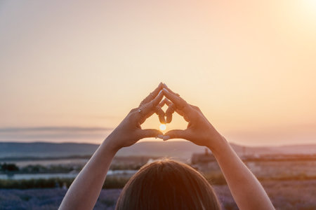 Sunset Hands House-shape Hope: Woman creates home symbol during golden hour sunrise.の写真素材