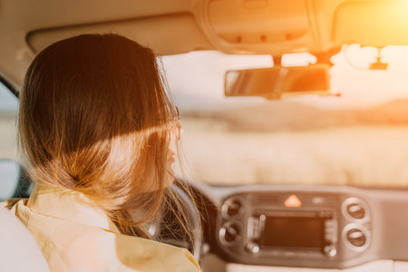 A woman in a yellow shirt is driving a car. She is wearing glasses and has her hands on the steering wheelの写真素材