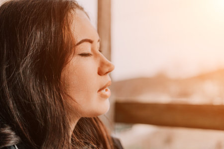 Woman, Window, Mountains - Closeup of a woman with her eyes closed standing in front of a window with a mountain view.の写真素材