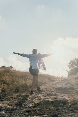 Man Running Hilltop Freedom - A man runs up a hilltop with his arms spread wide, symbolizing freedom and joy. The sun shines brightly in the background.の写真素材