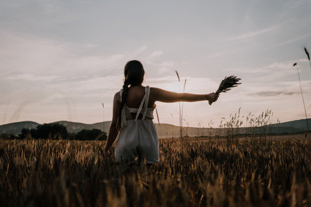 Woman in a Field at Sunset, Holding a Bouquetの写真素材