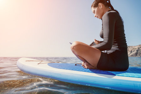 Woman Yoga Paddleboard Meditation Ocean Beach - A woman practices yoga on a paddleboard in the ocean on a sunny day.の写真素材