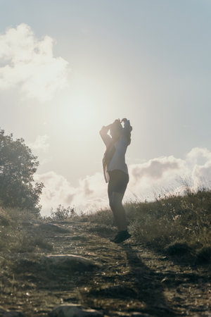 Woman Silhouette Mountain Landscape Sun A silhouette of a woman standing on a mountain with a bright sun and cloudy sky in the background.の写真素材