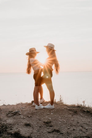 Two Women in Straw Hats Stand Back-to-Back, Silhouetted by the Sunsetの写真素材