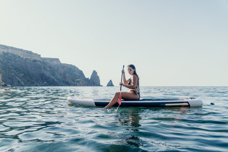 Woman Paddleboarding Ocean Coastline - A woman is paddleboarding in the ocean near a rocky coastline.の写真素材