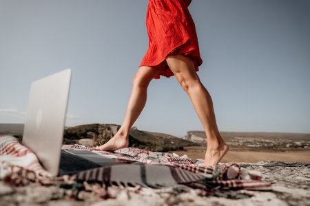 Woman in Red Dress Walking towards a Laptop on a Blanketの写真素材