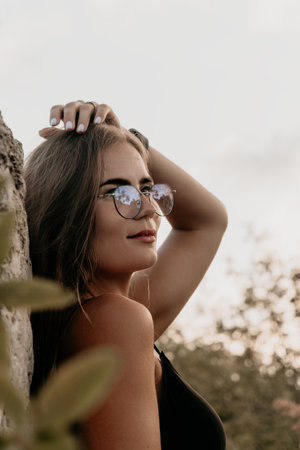 Woman Sunglasses Portrait Outdoors A woman wearing sunglasses looks up and to the right, her hand resting on her head. She is outdoors, likely in a natural environment. The photo is a portrait, focusing on the womans face and upper body.の写真素材