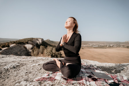 Woman Meditating on a Mountaintop with a Laptop and Blanketの写真素材