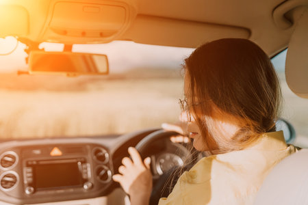 A woman in a yellow shirt is driving a car. She is wearing glasses and has her hands on the steering wheelの写真素材