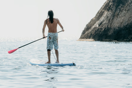 Man Sup Sea. Strong athletic man learns to paddle sup standing on board in open sea ocean on sunny day. Summer holiday vacation and travel concept. Aerial view. Slow motionの写真素材