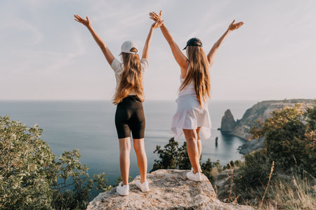Two Women Raise Their Arms on a Cliff Overlooking the Oceanの写真素材