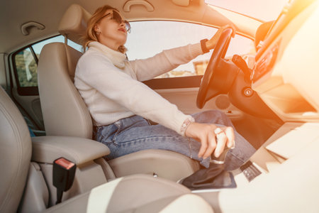 Woman Driving Car Gearshift Sunlight - Female driver behind the wheel of a car, shifting gears while the sun shines through the window.の写真素材