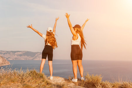 Two Women Raising Their Arms in Victory on a Cliff Overlooking the Oceanの写真素材