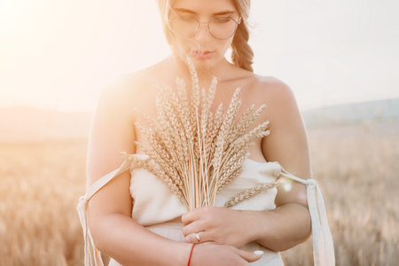 Woman wheat field. Agronomist, Woman farmer check golden ripe barley spikes in cultivated field. A woman is holding a bunch of wheat in her arms.の写真素材