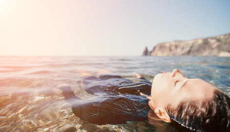 Woman Floating Ocean Water Relaxation - A woman relaxes in the ocean with her eyes closed, enjoying the warm sunshine and calm water.の写真素材