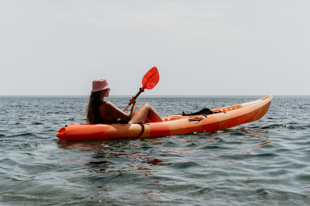 Kayaking Woman Ocean Paddle - A woman wearing a pink hat paddles a red kayak in the ocean on a cloudy day.の写真素材
