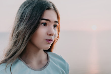 Portrait of a Young Girl with Long Hair Against a Blurry Sunset Backgroundの写真素材