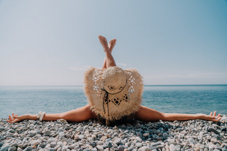 A woman is laying on the beach wearing a straw hat and looking at the oceanの写真素材